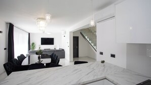 Una cocina moderna con encimera de mármol, una zona de comedor con sillas negras y una escalera que sube a otro nivel.