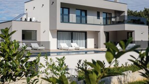 Una casa moderna de dos pisos con piscina, ventanas amplias y un balcón.