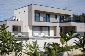 Ein modernes, zweistöckiges Haus mit Swimmingpool, großen Fenstern und einem Balkon.