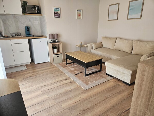 Un espace de vie compact comprenant un coin cuisine, un canapé, une table basse et une petite table d’appoint.