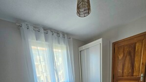 Ein Schlafzimmer mit Bett, einem Fenster mit Vorhängen, einer Tür und einer Hängelampe.