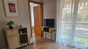 Ein Zimmer mit einem Holztisch, einem Fernseher, einer Zimmerpflanze und einem gerahmten Bild an der Wand.