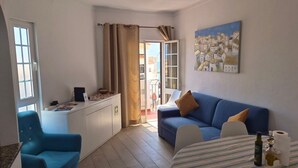 A room with a blue sofa, a small table with a striped tablecloth, a desk with a computer, and a painting on the wall. - Al Mare Ocean View (Albufeira)