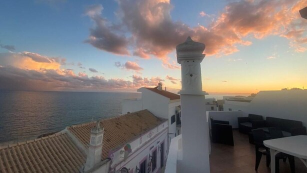 A rooftop terrace with a view of the sea, a white building with a tower, and outdoor furniture. - Al Mare Ocean View (Albufeira)