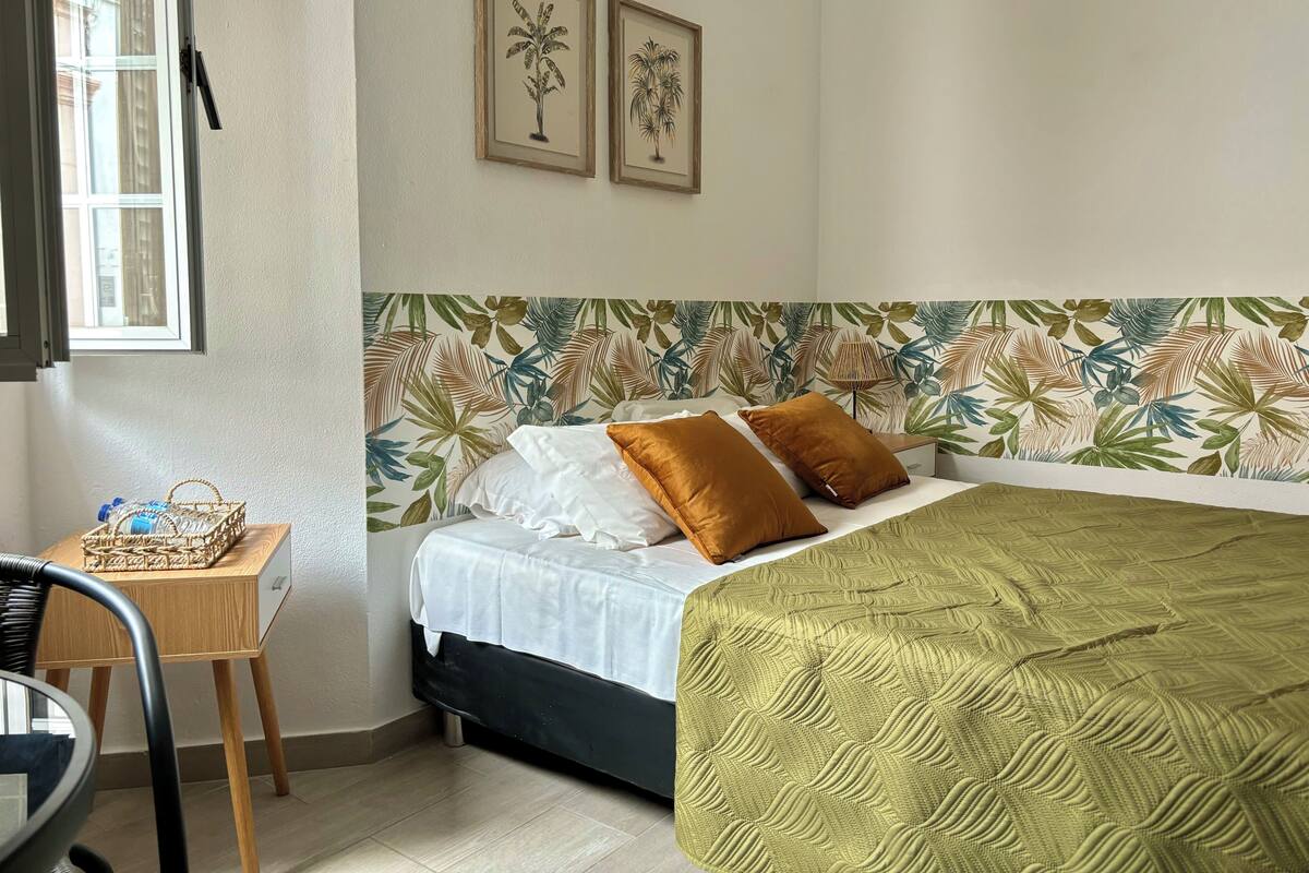 Une chambre à coucher comprenant un lit, une table de chevet, une chaise, une fenêtre et deux tableaux encadrés accrochés au mur.