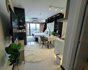 A modern hotel room with a bed, a dining area, a small kitchen, and a balcony with a city view. - STUNNING STUDIO WITH AWESOME BALCONY & 65" TV &KARAOKE (Makati)