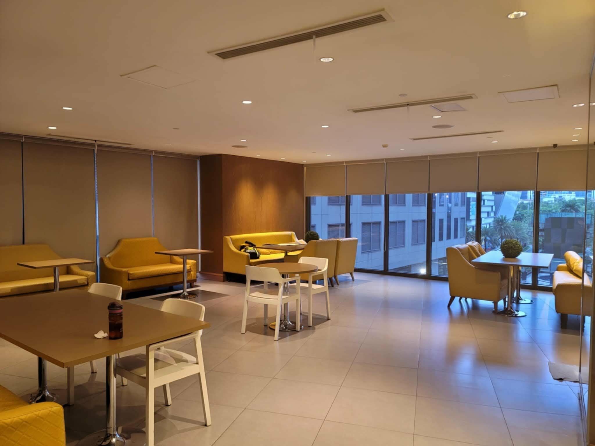 A modern hotel lobby with yellow seating, a coffee table, and a view of the cityscape through large windows.