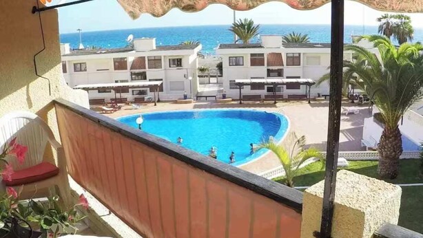 Una piscina con gente, vista al mar y edificios al fondo.