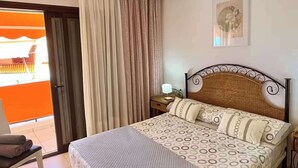 Una habitación de hotel con cama, mesita de noche, lámpara, silla y vistas al exterior.