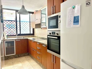 A kitchen with wooden cabinets, a built-in oven, a microwave, and a refrigerator. - Vera Mar 6 - Two Bed (Playa de las Américas)