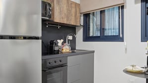 A compact kitchen with a refrigerator, oven, and microwave. There is a window with a blind, a small table with a vase, and a chair. - Prime Central Location Mahane Yehuda Market (Jerusalem)