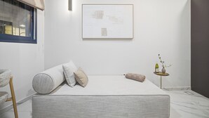 A minimalist bedroom with a bed, pillows, a small table with a vase, and a framed artwork on the wall. - Prime Central Location Mahane Yehuda Market (Jerusalem)