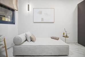 Ein schlicht eingerichtetes Schlafzimmer mit Bett, Kissen, einem kleinen Tisch mit Vase und einem gerahmten Kunstwerk an der Wand.