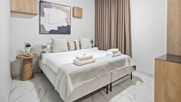 A modern bedroom with a bed, bedside tables, a wall-mounted artwork, and a window with curtains. - Prime Central Location Mahane Yehuda Market (Jerusalem)