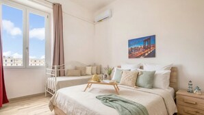 Een slaapkamer met een bed, nachtkastje, raam en een stadsgezichtschilderij.