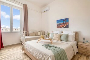 A bedroom with a bed, bedside table, window, and a cityscape painting. - ClickSardegna Central Park Penthouse in Alghero with parking for 9 guests (Alghero)