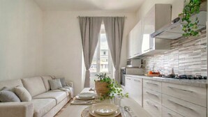 Een moderne keuken met witte kastjes, een eettafel gedekt met borden, en een bank in de woonkamer.
