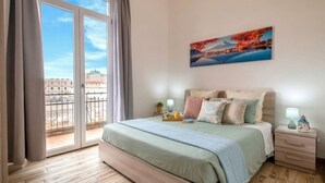 Een slaapkamer met een groot bed, een nachtkastje, een lamp, een schilderij en uitzicht door een schuifdeur.