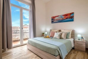 A bedroom with a large bed, a nightstand, a lamp, a painting, and a view through a sliding door. - ClickSardegna Central Park Penthouse in Alghero with parking for 9 guests (Alghero)