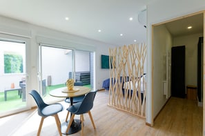 A modern interior with a round table, two chairs, a sofa, and a decorative wooden partition. - Studio Sable - Private Jacuzzi - Portbail sur mer center - Swimming pool access (Port-Bail-sur-Mer)