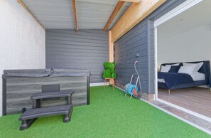 Un espacio exterior techado con un banco, una silla verde y un carrete de manguera.