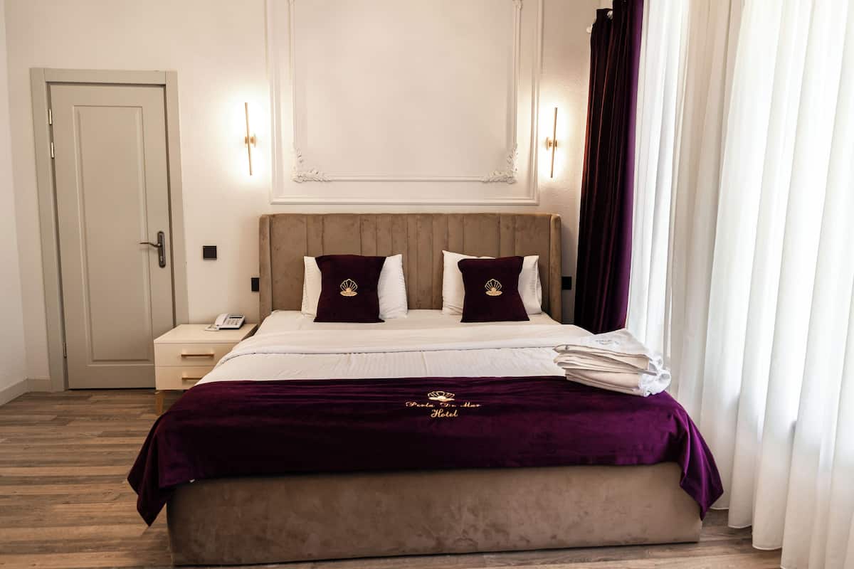 A hotel room with a large bed, a bedside table, a nightstand, and a door.