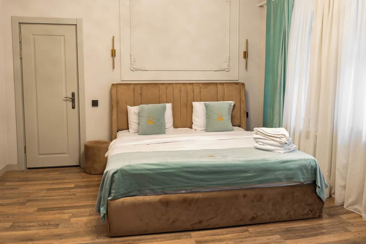 A bedroom with a wooden headboard, a bed with a green and white bedspread, two pillows, a bedside table, and a door.