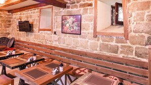 A rustic stone-walled room with wooden benches and tables, a framed fruit painting, and a mirror reflecting the room. - Governor Park Hotel (Baku)