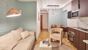 En moderne stue med sofa, sofabord, spiseplads med bord og stole, samt et køkken med komfur og ovn.