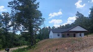 Une maison de plain-pied avec un toit à pignon, entourée d’arbres et bordée d’une allée en gravier.