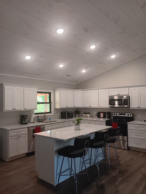 A modern kitchen with white cabinets, a central island with bar stools, a stainless steel oven, and a microwave.