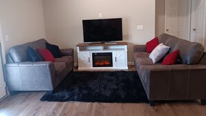 Un salon avec deux canapés en cuir, un téléviseur à écran plat, une cheminée et un tapis noir.