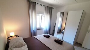 Ett hotellrum med en säng, ett nattduksbord, en spegel och ett fönster med gardiner.