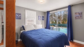 A bedroom with a large bed, a window with a view of a swimming pool, and a door leading to another room. - Cozy Muskegon Getaway Near Lake Michigan with Pool (Muskegon)