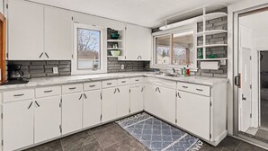 A modern kitchen with white cabinetry, a built-in stove, and a window overlooking the backyard. - Cozy Muskegon Getaway Near Lake Michigan with Pool (Muskegon)
