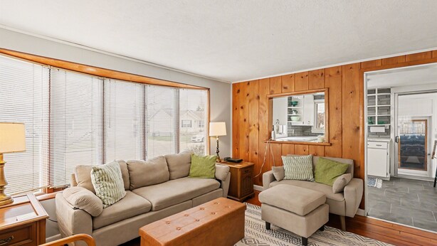A living room with a sofa, ottoman, and a small table with a lamp. There is a kitchen visible through an open door. - Cozy Muskegon Getaway Near Lake Michigan with Pool (Muskegon)