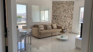 Un salon moderne avec un canapé beige, une table basse en verre et une vue sur la ville grâce à de grandes fenêtres.