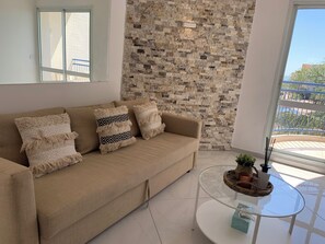 Una sala de estar moderna con un sofá color beige, cojines estampados, una mesa de centro de vidrio y una pared de piedra.