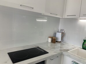 Una cocina moderna con armarios blancos, una placa de inducción negra y una encimera de mármol.