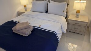 Un lit bien fait, avec une literie blanche rehaussée d’une touche de bleu, flanqué de deux tables de chevet surmontées de lampes, dans une pièce propre et épurée.
