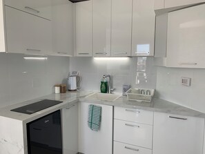Cocina moderna con armarios blancos, horno empotrado y encimera con hervidor y jabón para lavar platos.