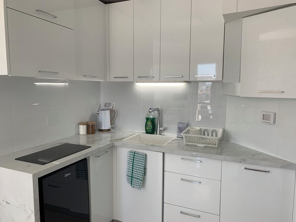 A modern kitchen with white cabinets, a built-in oven, and a countertop with a kettle and dish soap.