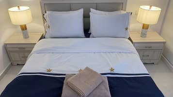 Een keurig opgemaakt bed met witte lakens en twee kussens, aan weerszijden geflankeerd door nachtkastjes met lampen, in een kamer met een strak, minimalistisch design.