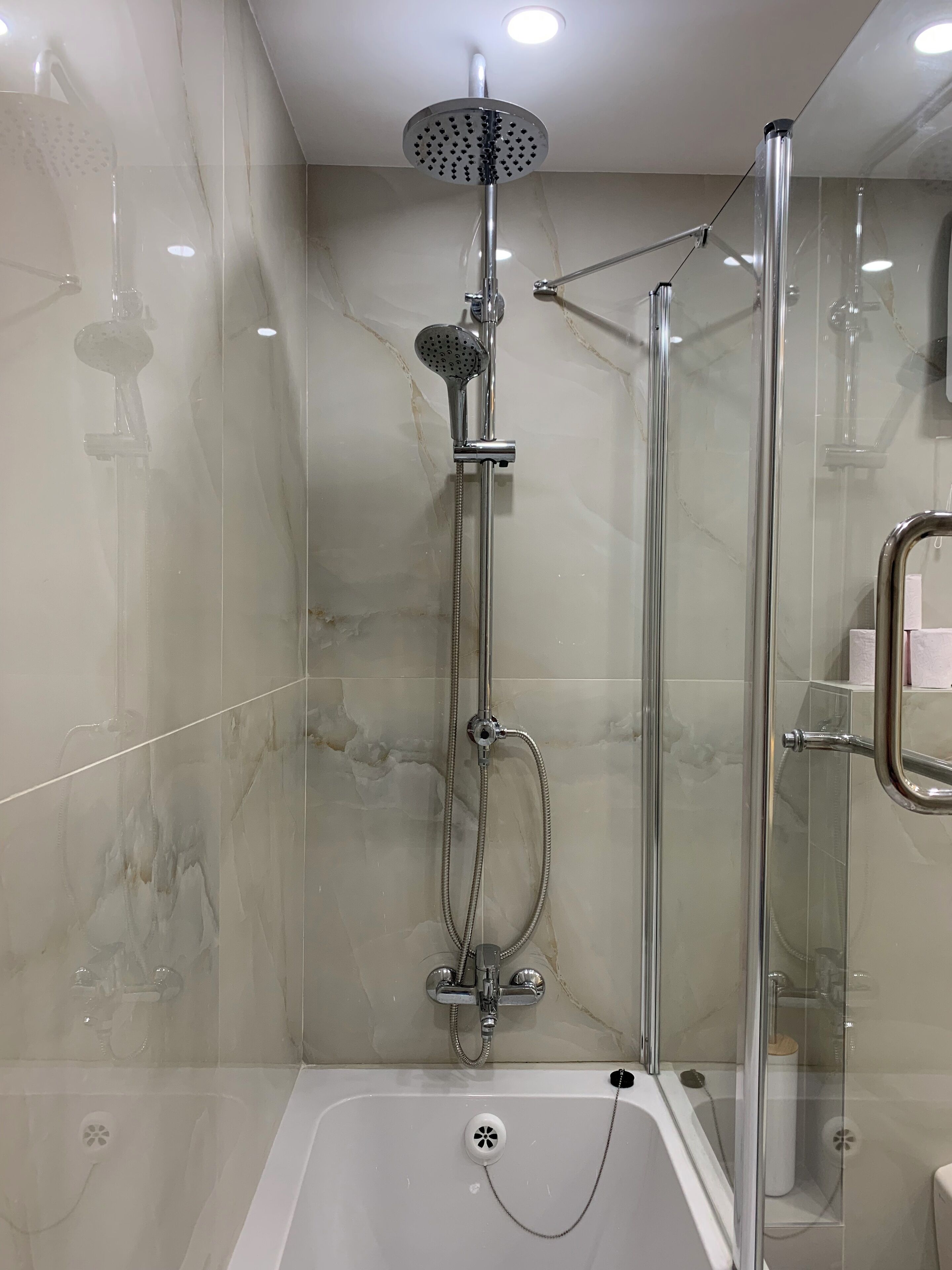 Une cabine de douche moderne dotée d’une porte en verre, d’un pommeau de douche à main et d’un autre pommeau de douche à main fixé au mur.