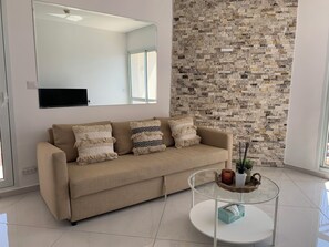Una sala moderna con un sofá color beige, una mesa de centro de vidrio y una pared de piedra.