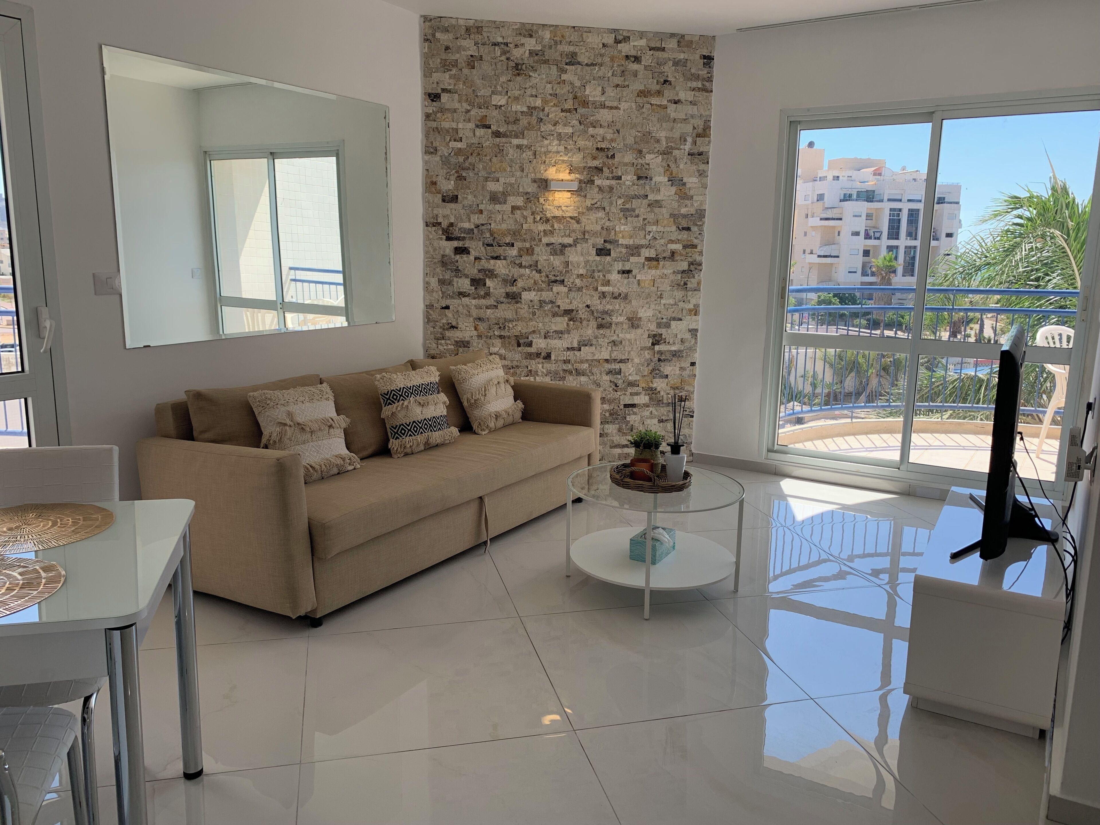 A modern living room with a beige sofa, a glass coffee table, and a stone wall.