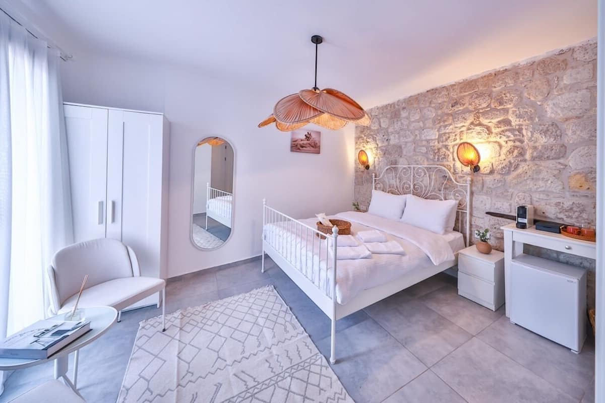 A bedroom with a bed, a white wardrobe, a chair, a desk, and a stone wall.