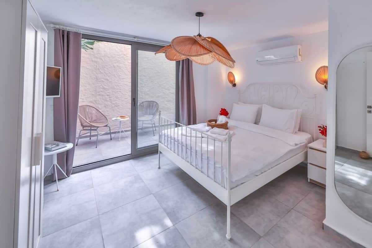 A bedroom with a bed, a chair, a table, and a balcony.