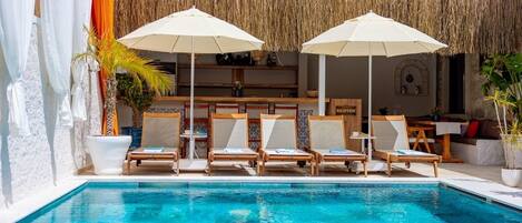 A pool area with lounge chairs and umbrellas, a reception desk, and a thatched roof structure.