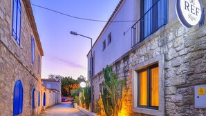 Una calle adoquinada estrecha con edificios de piedra, un cartel que dice 'REF Kayici' y un jardín de cactus.